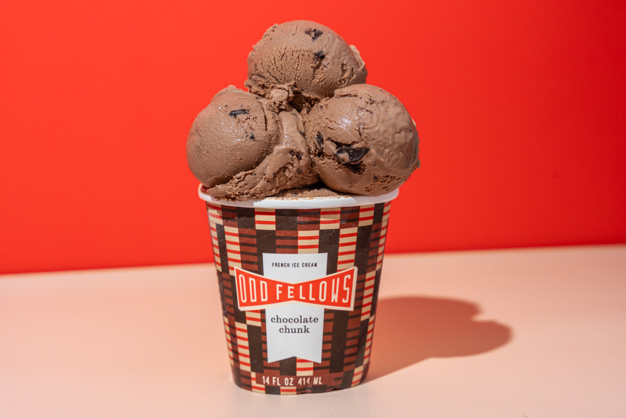 A cup of chocolate chip ice cream from Odd Fellows with three scoops against an orange background